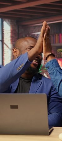 Black freelancing couple doing a high five to celebrate their achievement, completing tasks to ensure successful project. Young man and woman feeling pleased with their cooperation. Camera A.