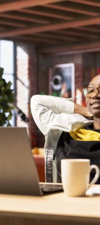 Joyous woman laying down on desk chair, relaxing at home, watching TV show on laptop. Smiling person sitting back and enjoying leisure time in apartment, consuming entertainment media content